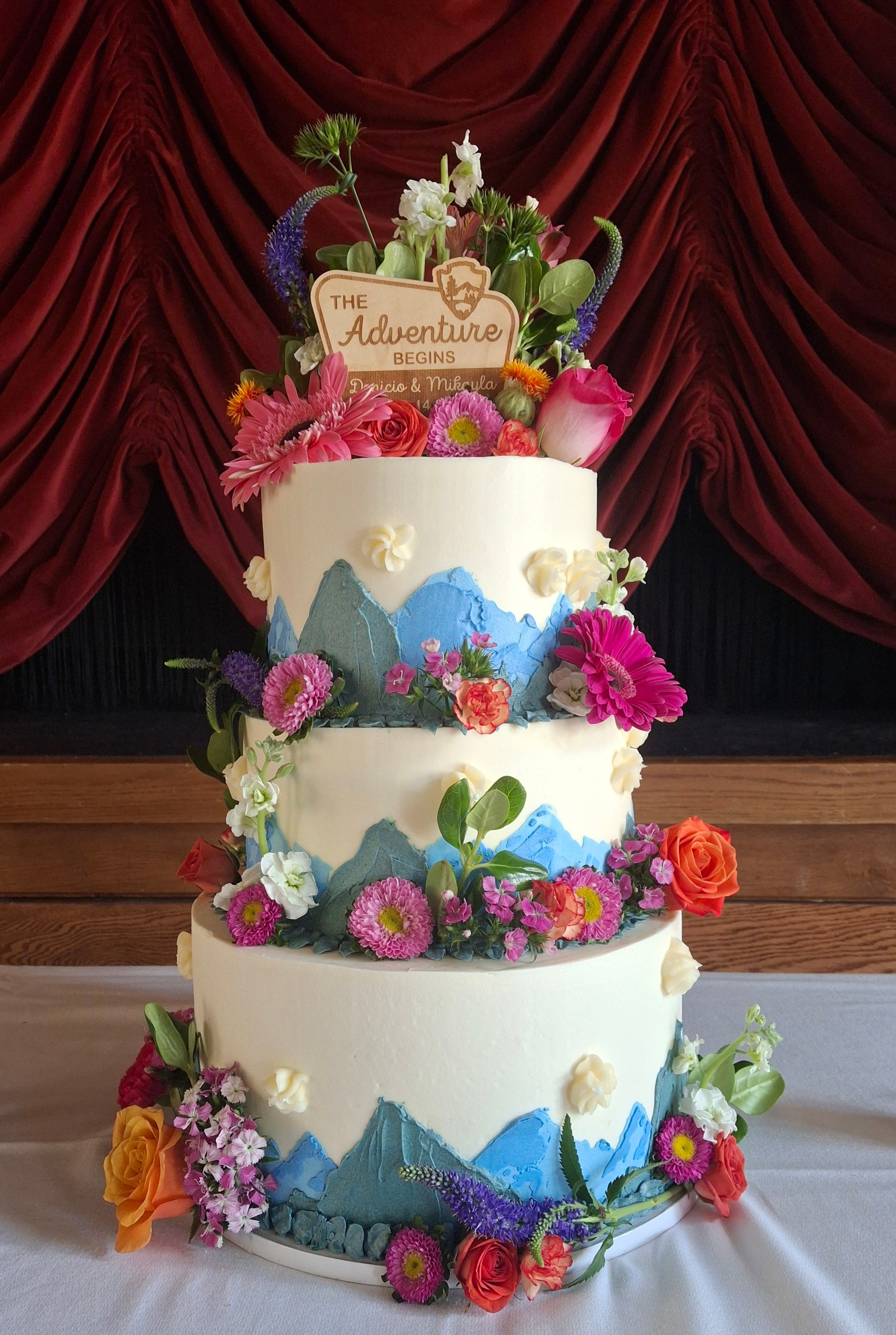 Four-tiered wedding cake with mountain scenery and colorful flowers