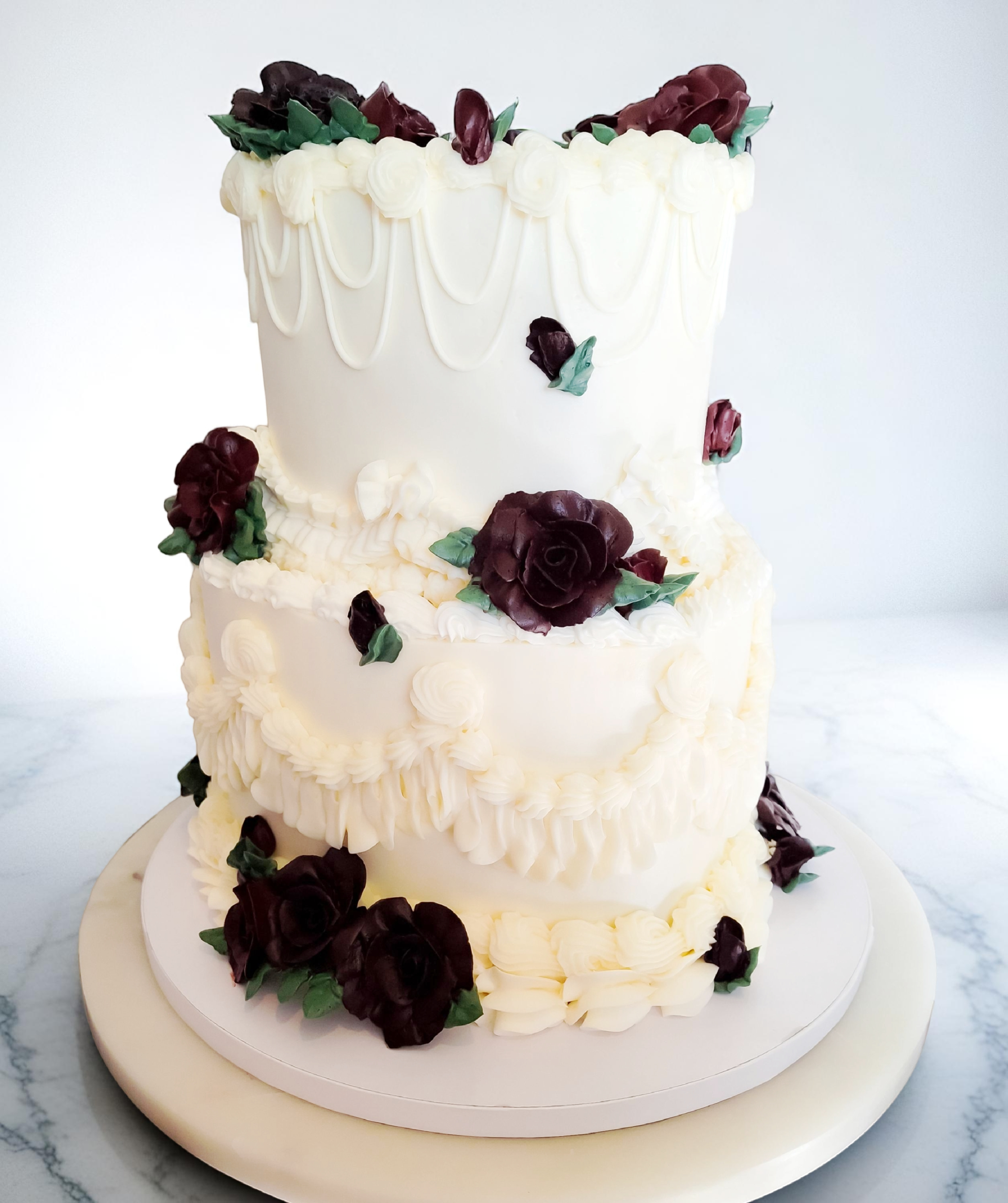 Two-tiered white cake with burgundy roses and elegant piped swag details